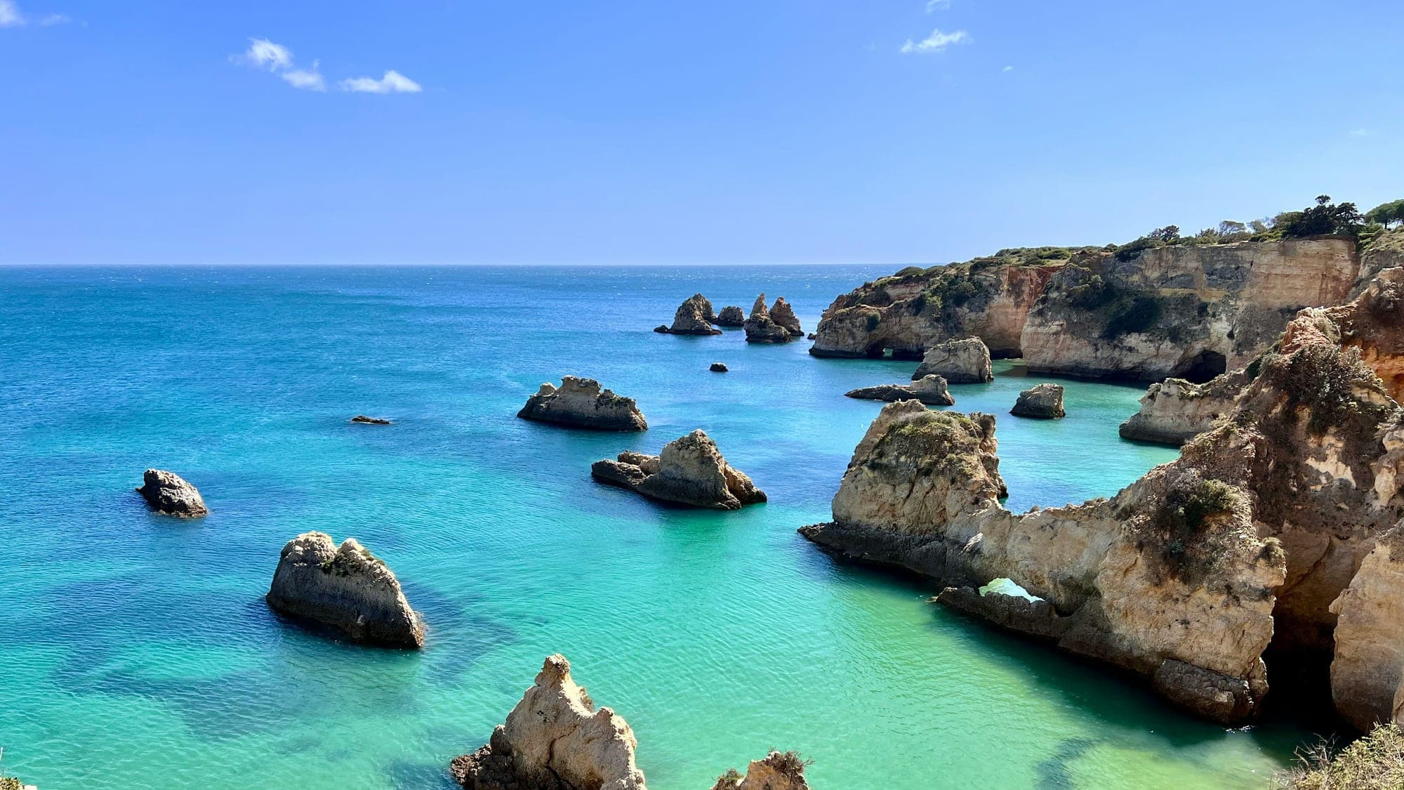 Falésias douradas e rochedos sobre águas turquesa na costa do Algarve