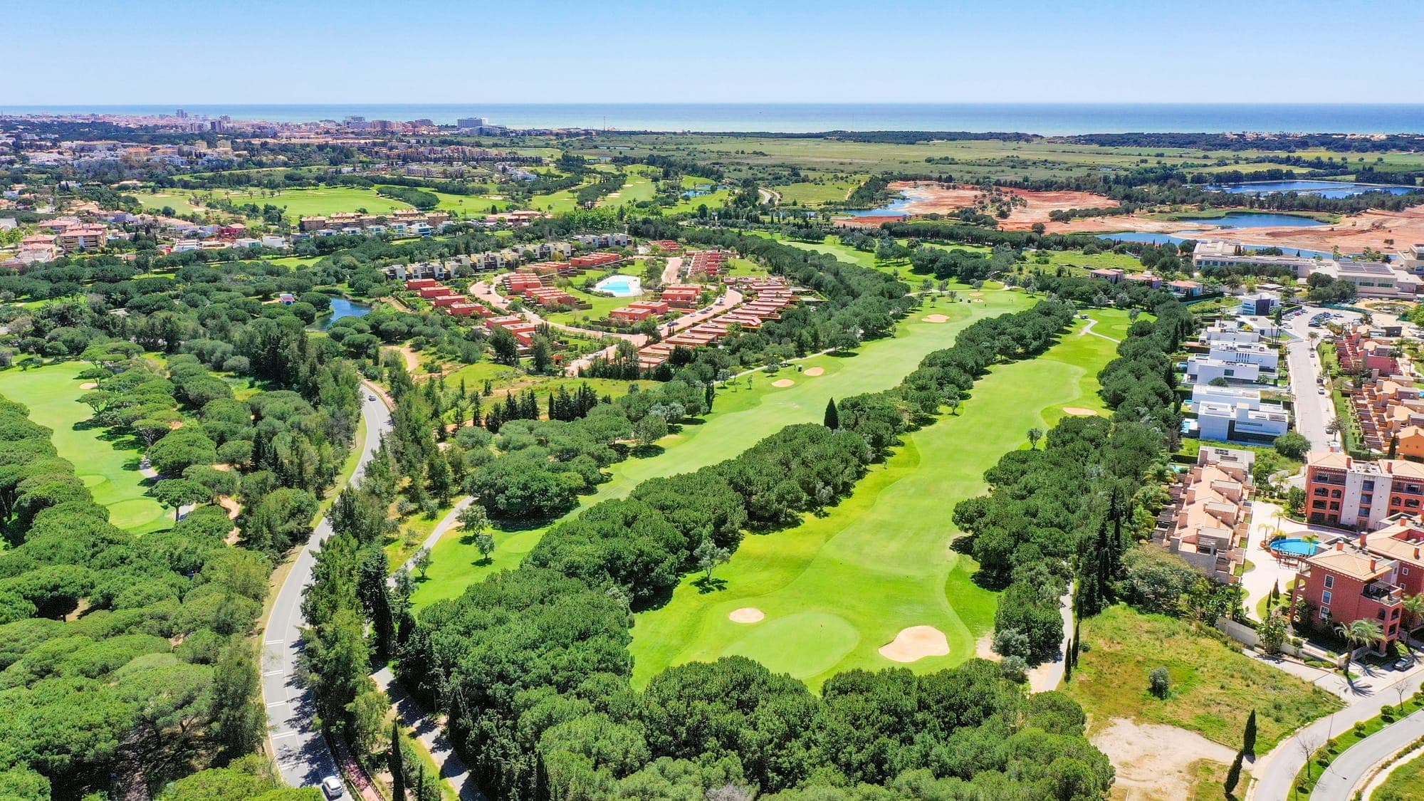 Vista aérea de um campo de golfe no Algarve, entre pinheiros-mansos, com o mar ao fundo
